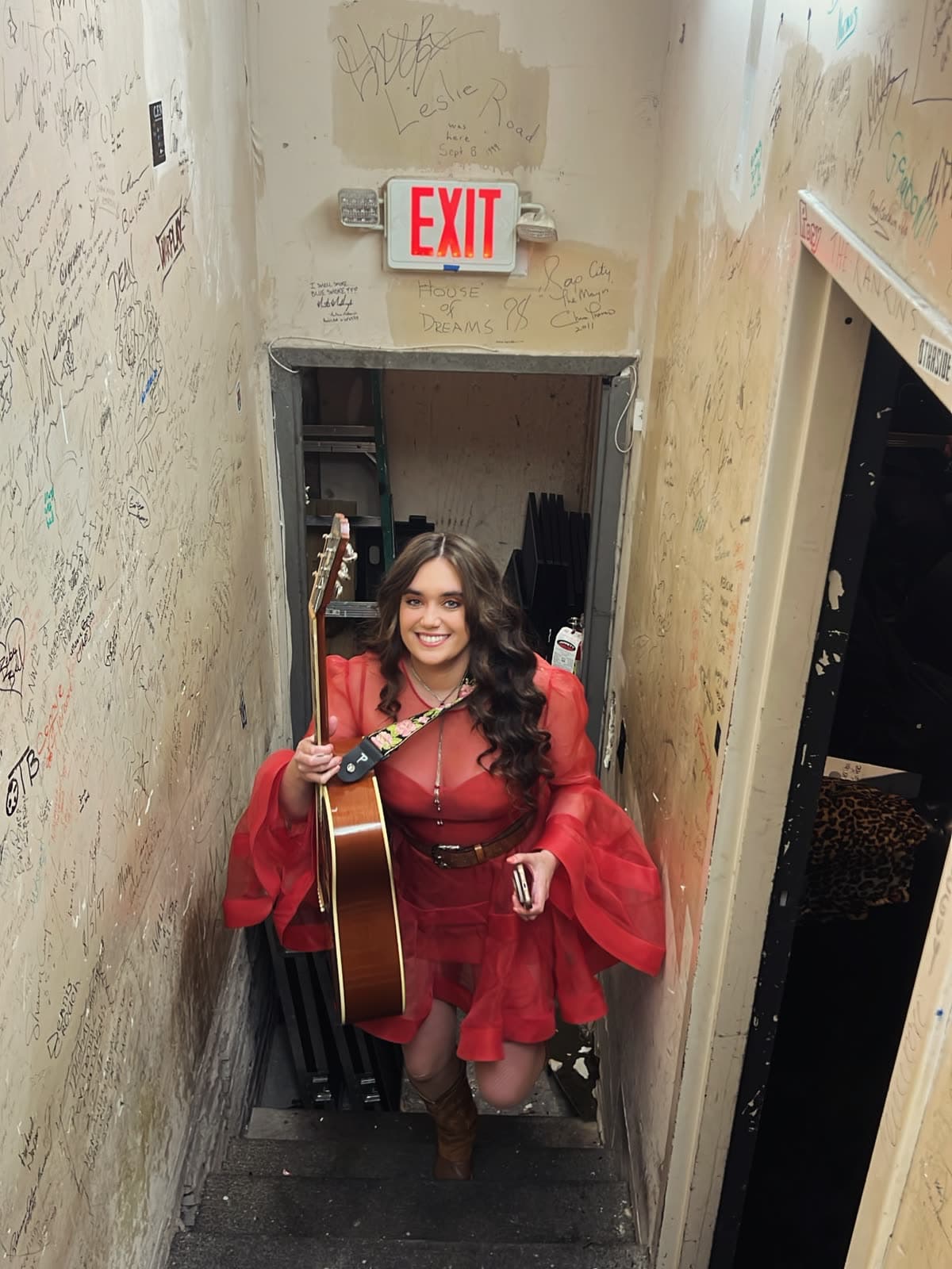 Belles in a red dress with an acoustic guitar backstage