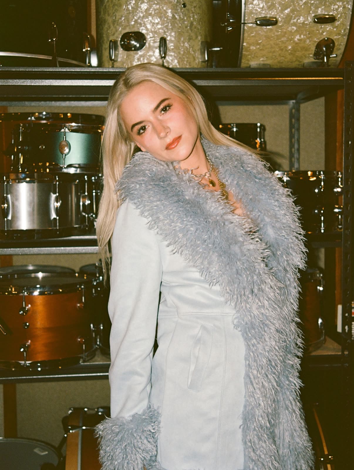 Felicity in a pale blue coat with a fur collar in a drum storage room